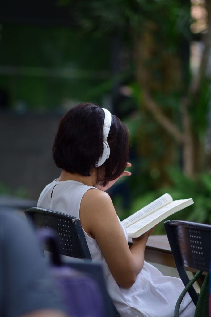 Foto de Sóc Năng Động: https://www.pexels.com/es-es/foto/mujer-leyendo-un-libro-mientras-lleva-auriculares-al-aire-libre-34239588/